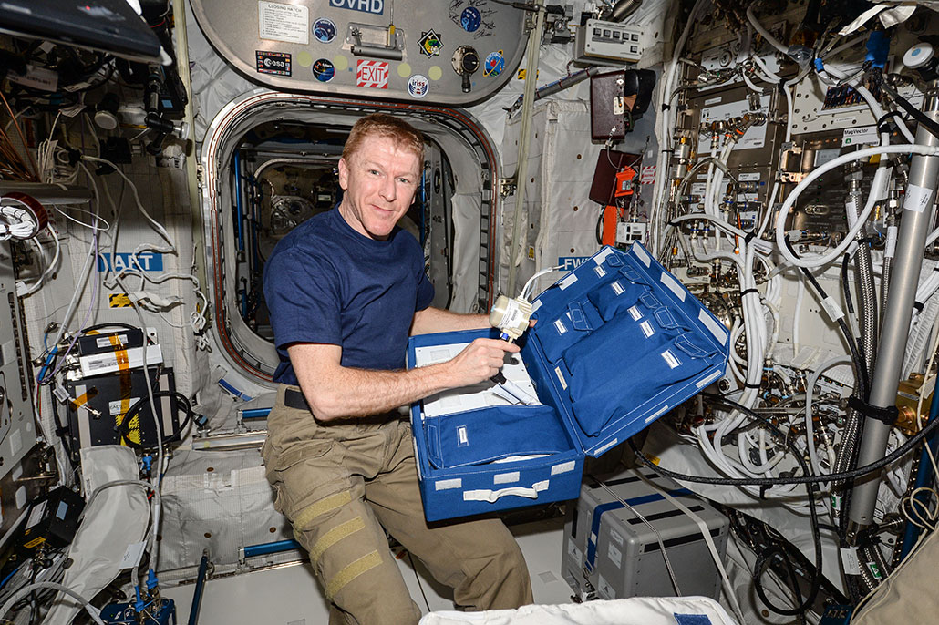 una foto de un astronauta masculino sosteniendo un dispositivo de medición mientras flota en la Estación Espacial Internacional