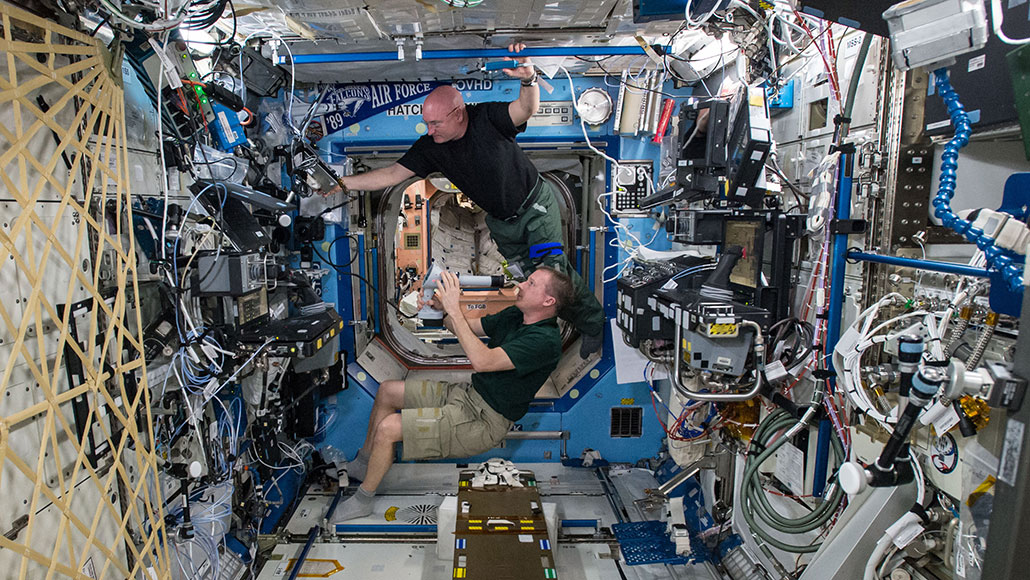 una foto de dos astronautas masculinos haciéndose exámenes de la vista mientras flotan dentro de la Estación Espacial Internacional