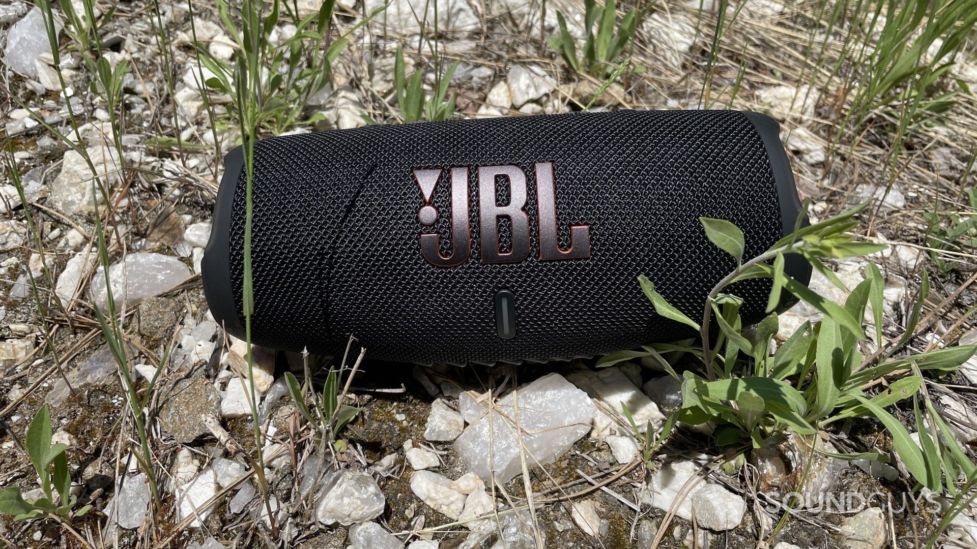 JBL Charge 5 descansando sobre rocas y hierba.