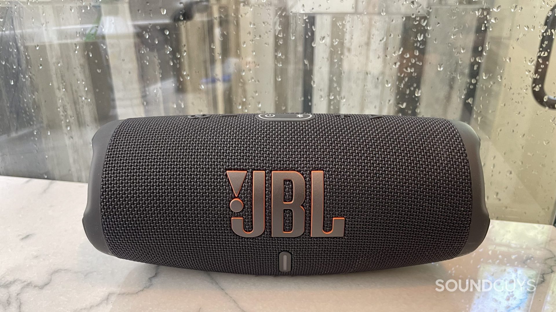 El altavoz Bluetooth JBL Charge 5 descansa sobre un mostrador con gotas de lluvia en una ventana detrás de él.