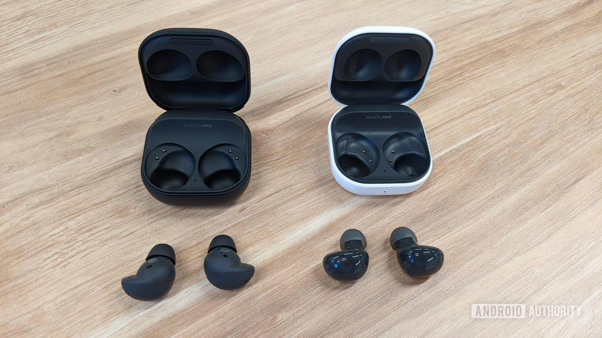 Los Samsung Galaxy Buds 2 Pro en grafito sentados fuera de su estuche a la izquierda de los Galaxy Buds 2 en grafito fuera de su estuche (blanco) sobre una mesa.