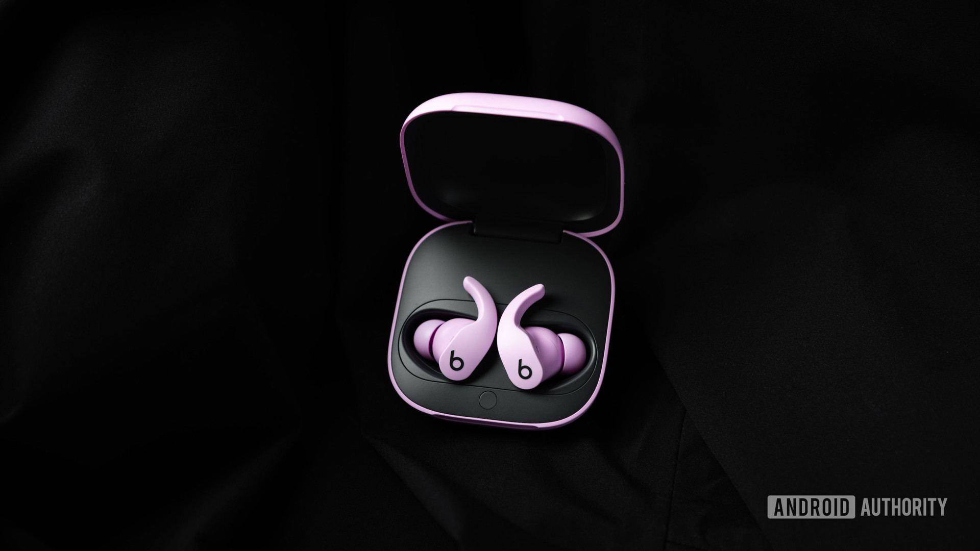 Los audífonos inalámbricos verdaderos con cancelación de ruido Beats Fit Pro en púrpura se encuentran en el estuche de carga abierto sobre un fondo de tela negra.